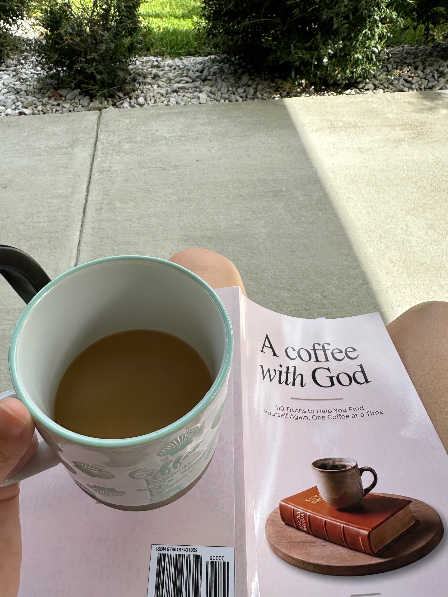 Morning coffee in a floral mug resting on the devotional book A Coffee with God, enjoyed outside in the sunshine
